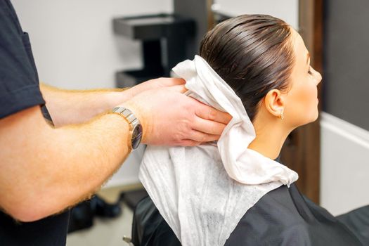 A male hairdresser's hands wipe the hair of a female client with a white towel after shampooing in a beauty salon
