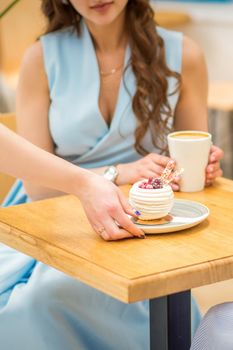 The waitress's hand puts the piece of cupcake on the table at a cafe, woman hand is putting round little pastry on the table on a background of a female in a blue dress