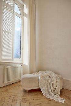 Comfortable ottoman with soft white coverlet placed near window and radiator in light room