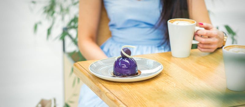 Young woman with cup of coffee and piece of cake sitting at the table in a cafe outdoors