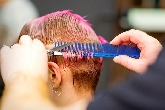 Young caucasian woman with pink hair getting a short haircut by a male hairdresser's hands in a hairdressing salon