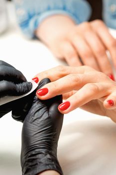 Closeup of manicure master in black gloves wiping the female red nails with a paper napkin in the beauty salon
