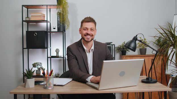 Businessman freelancer in suit enters office workplace, working on laptop computer at desk. Professional manager freelancer man works on notebook, sends messages makes online purchases watching movies