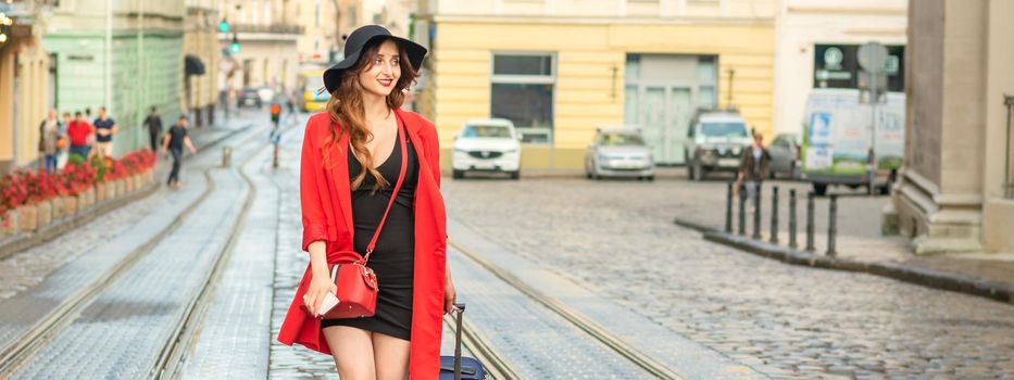 Beautiful young caucasian woman walks with a suitcase on a wet tram track in the European city