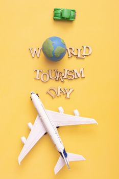 World Tourism Day text from wooden letters with globe, car and airplane on yellow background. Top view, flat lay.
