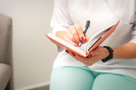 Close up of female doctor therapist writes notes in a medical notepad sitting in medical office