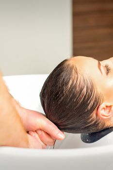 Male hairdresser washing hair in the sink to the female client before making hairstyling in a beauty salon