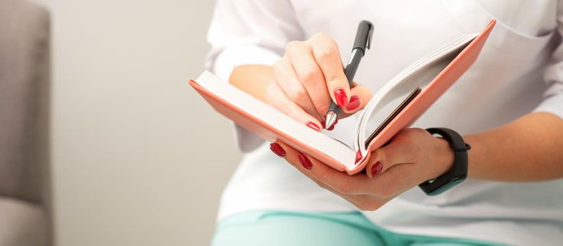 Close up of female doctor therapist writes notes in a medical notepad sitting in medical office