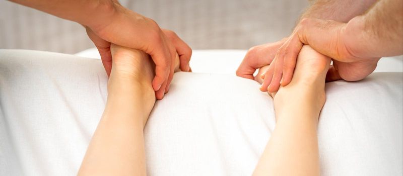 Two masseurs massaging feet of young woman in spa beauty salon