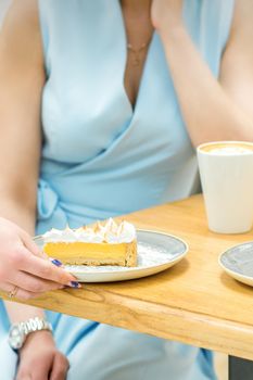 The waitress's hand puts the piece of cupcake on the table at a cafe, woman hand is putting round little pastry on the table on a background of a female in a blue dress