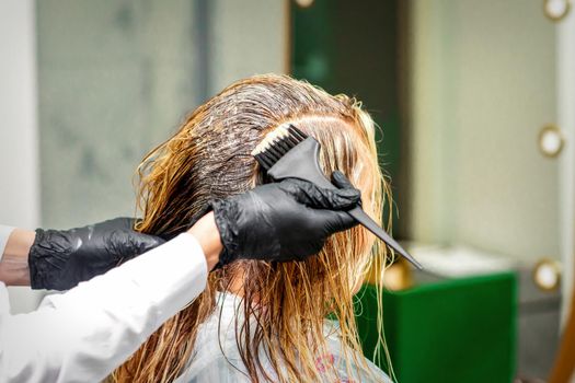Hand of a hairdresser in black gloves applying dye to the female hair in a beauty salon