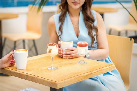 Hands of a young woman holding a cup of coffee with different cocktails on the table at the cafe