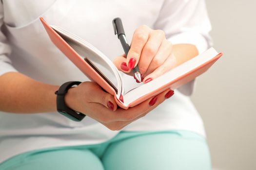 Close up of female doctor therapist writes notes in a medical notepad sitting in medical office