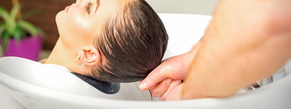 Male hairdresser washing hair in the sink to the female client before making hairstyling in a beauty salon