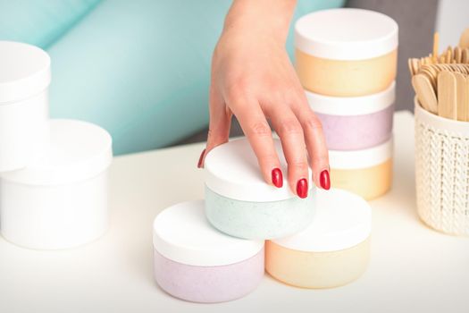 Beautician's hand takes jar with cosmetics from table offering and selling cosmetic products, moisturizing cream, wax paste
