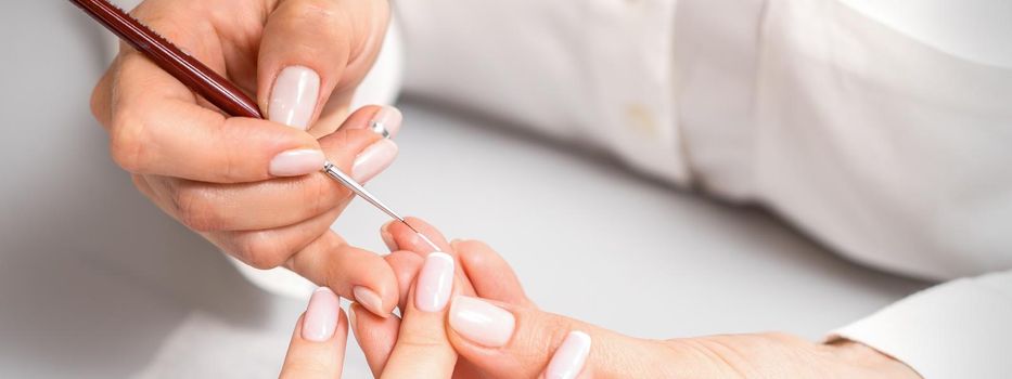 French manicure. Manicure master drawing white varnish on the nail tip with a thin brush, close up