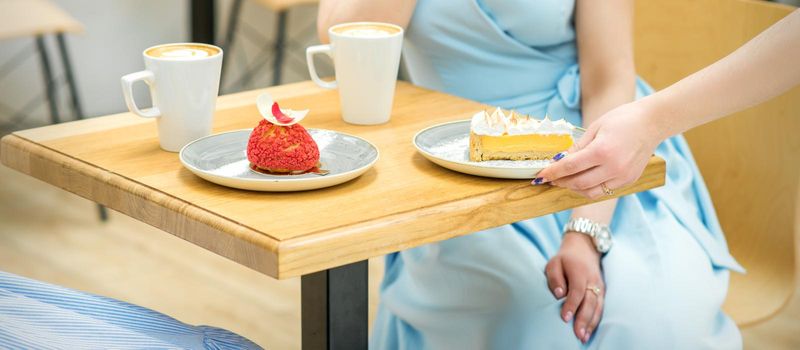 The waitress's hand puts the piece of cupcake on the table at a cafe, woman hand is putting round little pastry on the table on a background of a female in a blue dress