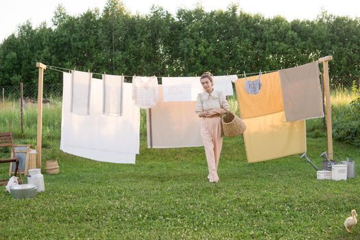 Laundry day. A woman hangs linen and towels on a tree in the courtyard of a village house. Summer cottage concept.