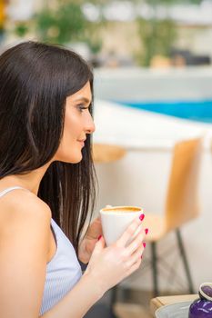 The side view of a young woman drinking coffee resting at the resort at a cafe outdoors