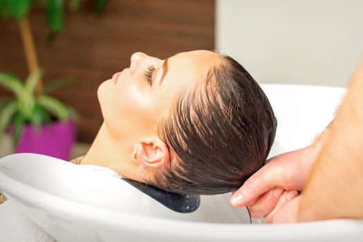 Male hairdresser washing hair in the sink to the female client before making hairstyling in a beauty salon