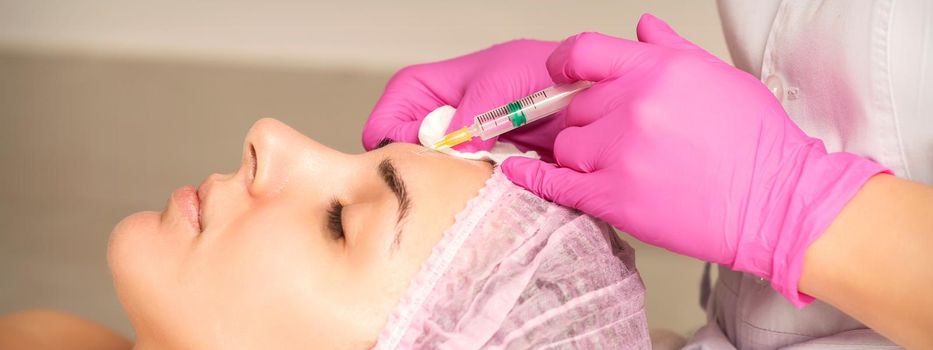 Young woman receiving an injection of anti-aging botox filler to the forehead from a cosmetologist in a beauty salon. Facial treatment injection