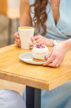 The waitress's hand puts the piece of cupcake on the table at a cafe, woman hand is putting round little pastry on the table on a background of a female in a blue dress