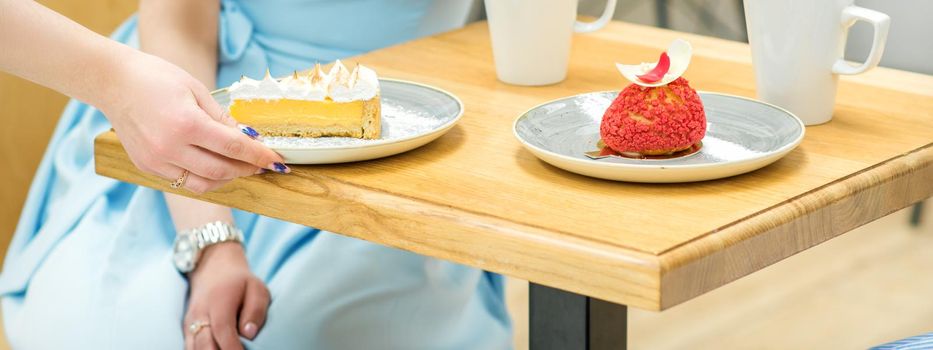 The waitress's hand puts the piece of cupcake on the table at a cafe, woman hand is putting round little pastry on the table on a background of a female in a blue dress