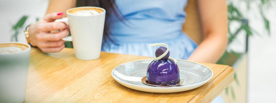 Young woman with cup of coffee and piece of cake sitting at the table in a cafe outdoors