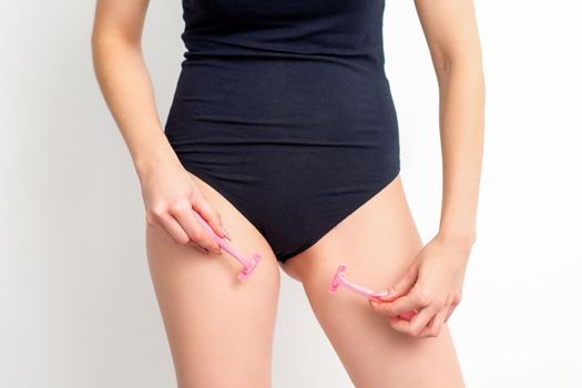 Young woman shaving crotch in bikini zone with two razors standing on white background, concept skincare and hair removal
