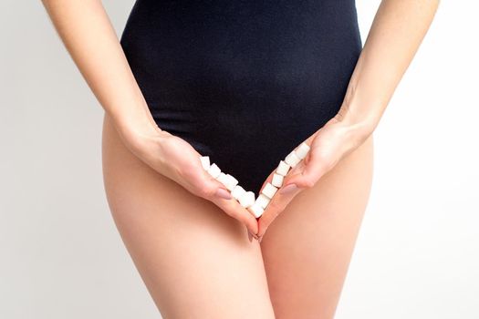 Woman holding sugar cubes on bikini zone, the concept of intimate depilation, problems of intimate hygiene