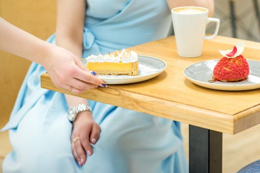 The waitress's hand puts the piece of cupcake on the table at a cafe, woman hand is putting round little pastry on the table on a background of a female in a blue dress