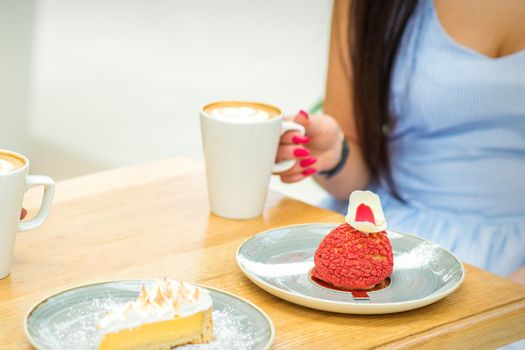 Young woman with cup of coffee and piece of cake sitting at the table in a cafe outdoors
