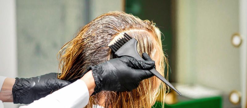 Hand of a hairdresser in black gloves applying dye to the female hair in a beauty salon