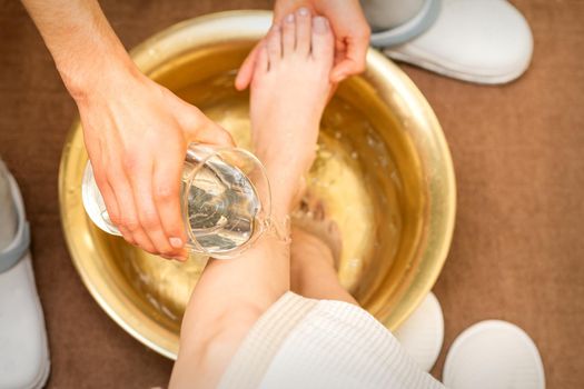 Top view of hands of masseur washing legs of a young woman in a golden bowl at beauty spa salon