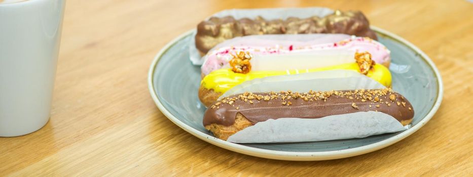 Several different eclairs on a plate are on the table with a cup of coffee in a cafe