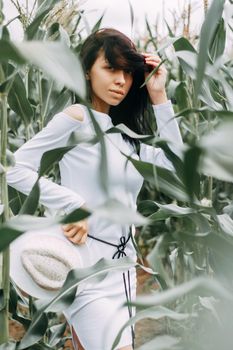 A brunette girl in a white dress in a cornfield. The concept of harvesting.