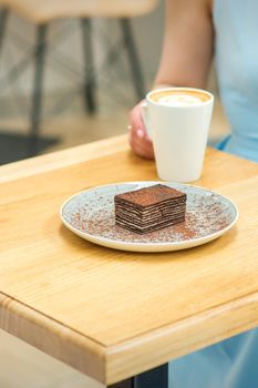 Young woman with cup of coffee and piece of cake sitting at the table in a cafe outdoors