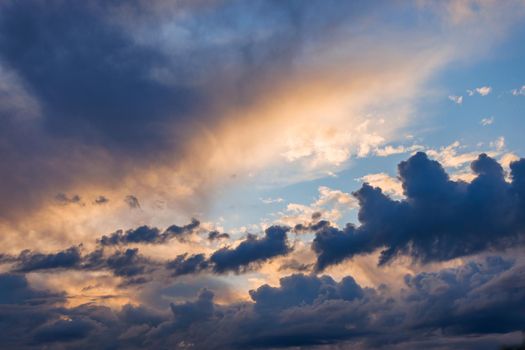 Cumulus clouds on evening sky backlit with sunset. Captured with 70mm lens on 35mm full-frame sensor camera.