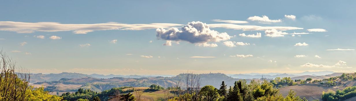 View of the Montefeltro hills and mountains from Belvedere Fogliense in the Marche region of Italy, at evening, under a cloudy sky.