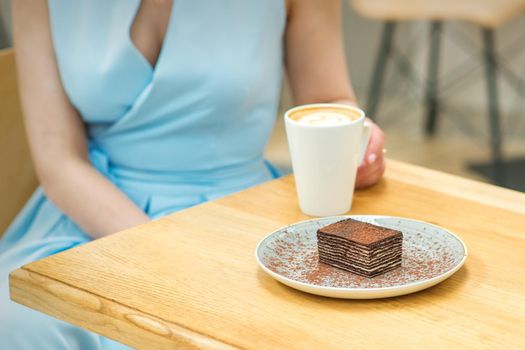 Young woman with cup of coffee and piece of cake sitting at the table in a cafe outdoors