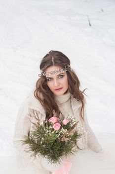 Beautiful bride in a white dress with a bouquet in a snow-covered winter forest. Portrait of the bride in nature.Beautiful bride in a white dress with a bouquet in a snow-covered winter forest. Portrait of the bride in nature.