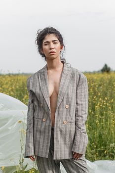 An Asian model poses in a field of yellow flowers for a clothing brand, polyethylene is the main props for a photo shoot. The concept of manufacturing clothing from recycled plastic. A woman in a pantsuit is standing on a plastic bag.