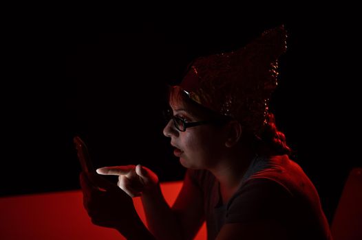 Paranoid caucasian woman using smartphone wearing tinfoil hat. Conspiracy theory