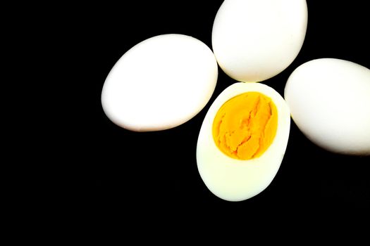 White eggs, one of them boiled and broken in a half on black background