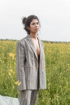 An Asian model poses in a field of yellow flowers for a clothing brand, polyethylene is the main props for a photo shoot. The concept of manufacturing clothing from recycled plastic. A woman in a pantsuit is standing on a plastic bag.