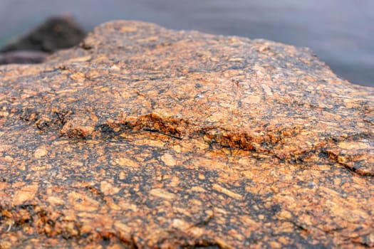 a large stone on the shore of the bay. textured surface of a huge natural brown-red stone