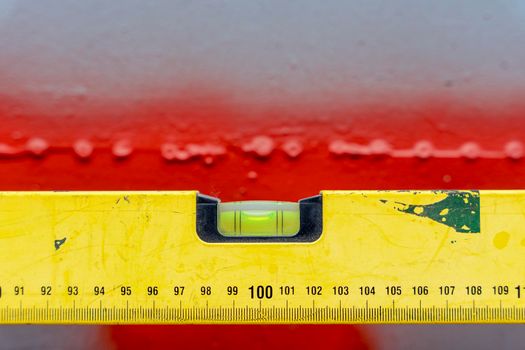 an iron yellow bubble construction level with a length marking on a red-gray background in a horizontal position. Close-up. Space for copying. Leader. Construction and engineering equipment. Measure