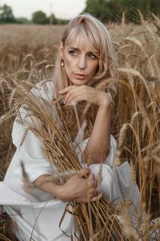 A blonde woman in a long white dress walks in a wheat field. The concept of a wedding and walking in nature.