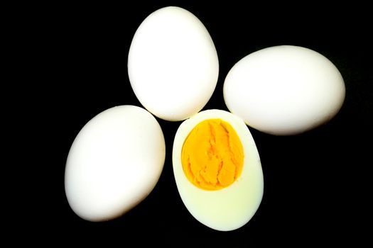 White eggs, one of them boiled and broken in a half on black background
