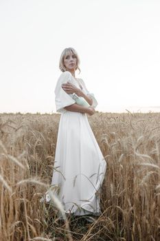 A blonde woman in a long white dress walks in a wheat field. The concept of a wedding and walking in nature.